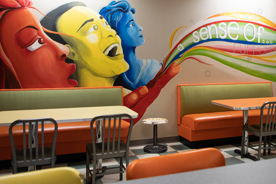 Cafe with mural of faces and swirling colors and colorful booths for seating